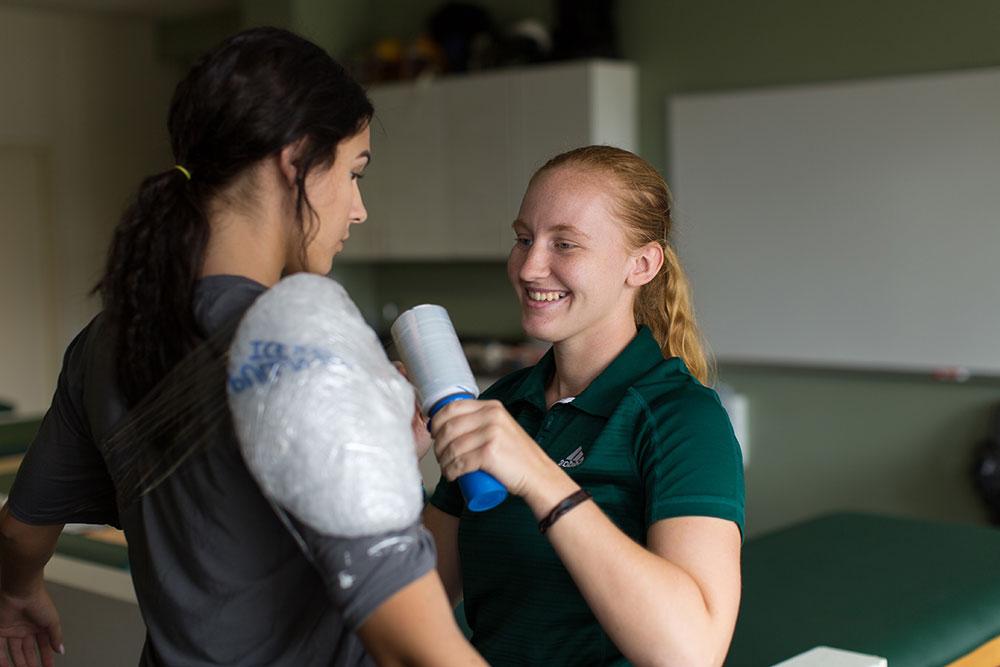 A volleyball player gets her shoulder wrapped by an athletic trainer.